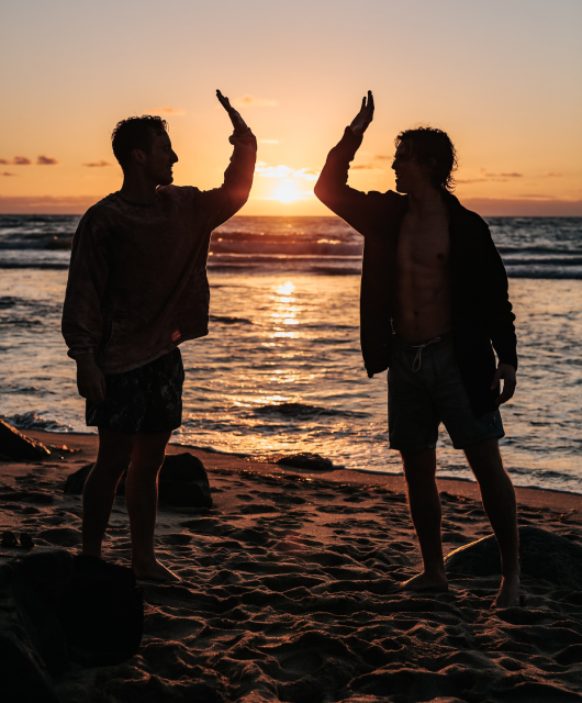 Landscape of a beach during a sunset, with two guys doing a highfive.